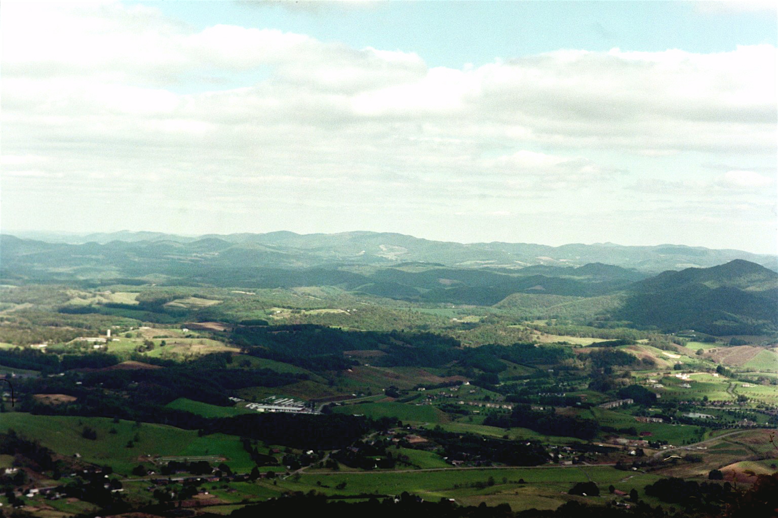 Vast rolling farmland patchwork across Ashe County, NC from a high overlook with layered ridgelines in the distance
